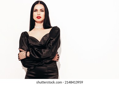 High fashion portrait of young beautiful brunette woman wearing nice trendy black evening dress and gloves. Sexy fashion vamp model posing in studio. Fashionable female isolated on white.With red lips