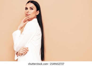 High fashion portrait of young beautiful brunette woman wearing nice trendy white suit. Sexy fashion model posing in studio. Fashionable female isolated on beige 