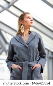 High Fashion Portrait Of Young Elegant Woman In Grey Coat, Black Pants, Black Ankle Boots And Gold Earrings