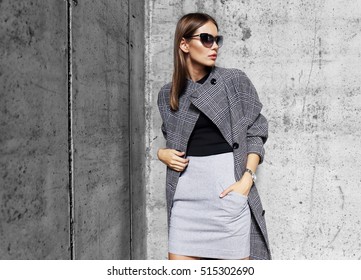 high fashion portrait of young elegant woman outdoor. Grey Ã?Â�oat, cat eye sunglasses, grey wall background
