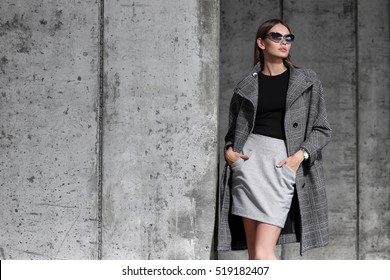 High Fashion Portrait Of Young Elegant Woman Outdoor. Grey Coat, Cat Eye Sunglasses, Grey Wall Background