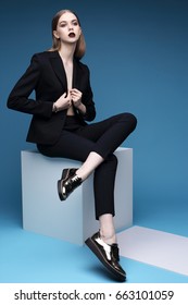 High Fashion Portrait Of Young Elegant Woman In Black Suit And Loafers. Studio Shot.