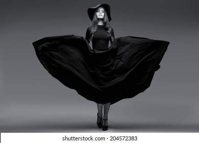 High Fashion Shot Of Elegant Woman In A Hat And Long Fluttering Dress. Black And White Image