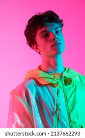 High Fashion Shot. Portrait Of A Handsome Male Model With Dark Wavy Hair Posing In Stylish Designer Jacket On A Bright Pink Background. 