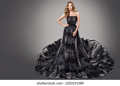 High Fashion Woman In Black Luxury Dress. Blonde Model In Long Glitter Tulle Gown. Women Party Make Up And Curly Hair Style Over Dark Gray Background