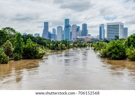 High and fast water rising in Bayou River with downtown Houston in background under cloud blue sky. Heavy rains from Harvey Tropical Hurricane storm caused many flooded areas in greater Houston area.