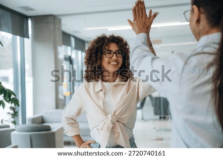 High five hands gesture. Two women are indoors in the modern hall of building at daytime.