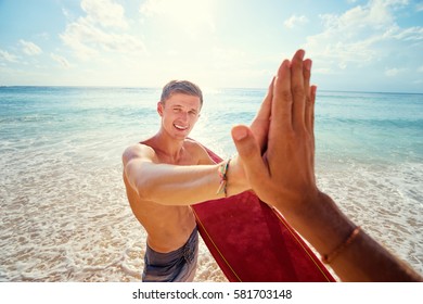 High five! Vacation and friendship. Handsome young man holding surfboard on the sunny beach. - Powered by Shutterstock