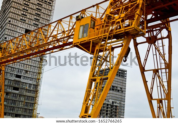 High heavy yellow metal iron load-bearing\
construction stationary industrial powerful gantry crane of bridge\
type on supports for lifting cargo on a modern construction site of\
buildings and houses.