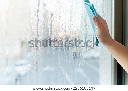 High humidity at home. Man wipes the window of his house with a sponge the water condensation on the glass.