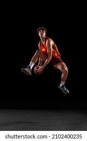 High jump. Full length portrait of basketball player training isolated on dark studio background. Tall muscular athlete jumping with ball. Sport, energy, power, results. Motion, activity, movement