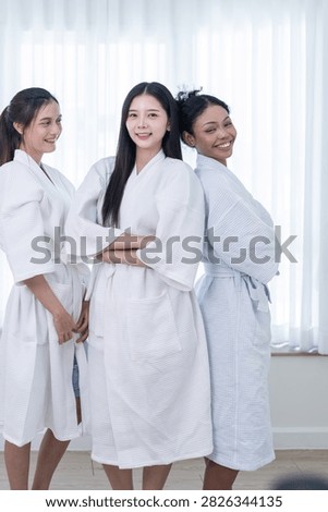 High key wellness image of three diverse female friends standing with folded arms in a team portrait, where the woman with voluminous curly hair rests her cheek against her friend.