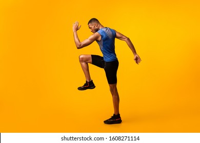 High Knees. Energetic afro man doing fitness exercise, lifting leg and waving arm, free space