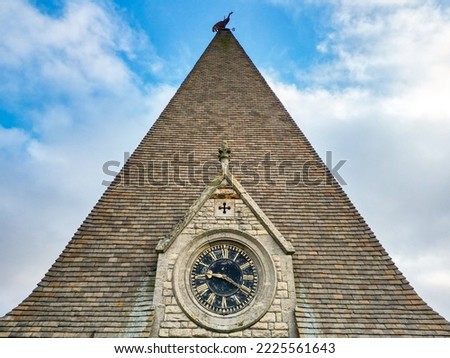 High level view of a large clock seen in a English clock tower with the church spire and metal weathercock atop.