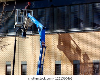 High Level Window Cleaning. High Pressure Water Jet Window And Facade Wash. Telescopic Arm. Cherry Picker. Safety Cage On Boom. Worker In Red Hardhat And In Harness. Commercial Facade Washing Concept
