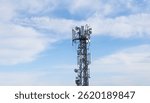 High metal antenna on blue sky background. Communication tower with many receivers and transmitters on it - base station.