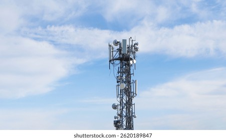 High metal antenna on blue sky background. Communication tower with many receivers and transmitters on it - base station.