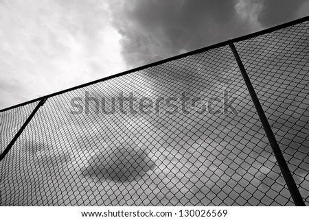 A high metal chain link fence against a stormy cloudy sky.