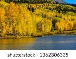 High mountain lake with wooden pier surrounded by changing yellow aspen trees on warm autumn afternoon