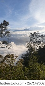High mountain view with rolling clouds, lush tropical vegetation, and distant peak under clear sky in tranquil nature scene