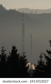 High old smokestack in industrial area and misty atmoshpere sunset on the background. Roznov pod Radhostem, Czech republic.