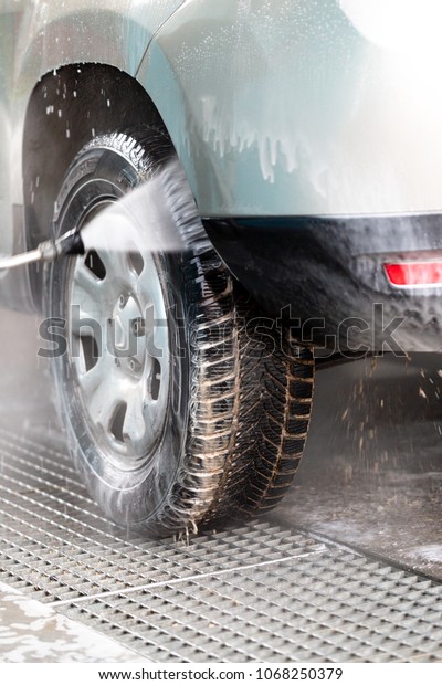 High pressure water stream washing\
a car at handwash car station. Vertical close up\
crop