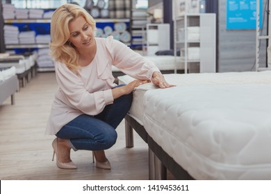 High Quality Home Goods Concept. Beautiful Elegant Mature Woman Shopping For Furniture At Department Store. Attractive Female Customer Examining Orthopedic Mattress At Furnishings Shop