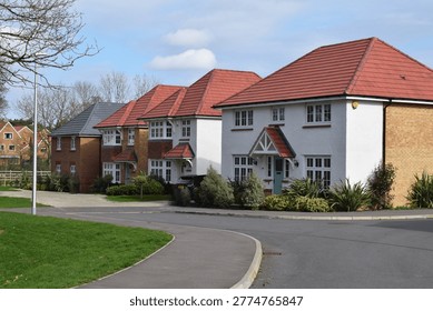 High quality housing development featuring beautiful detached houses with mixed roof tiles and varied facade materials, set within landscaped surroundings along a winding residential road. The scene shows a contemporary UK suburban estate with carefully planned architecture, varied housing designs, and integrated greenery, reflecting modern residential development and suburban planning.