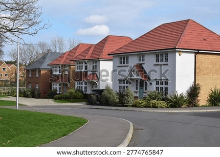 High quality housing development featuring beautiful detached houses with mixed roof tiles and varied facade materials, set within landscaped surroundings along a winding residential road. The scene shows a contemporary UK suburban estate with carefully planned architecture, varied housing designs, and integrated greenery, reflecting modern residential development and suburban planning.