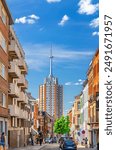 High residential building with spire and narrow street with parking cars in Leuven city center in sunny summer day, blue sky background, Flemish Region, Flemish Brabant province, Belgium