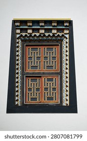 High resolution vertical closeup of a single trapezoid Tibetan window with carved geometric
lattice shutters and painted decorative frame on a white monastery wall