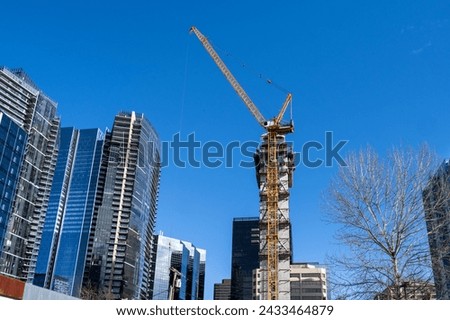 High rise cityscape of a modern downtown, tall crane and construction of a new skyscraper on a sunny blue sky day
