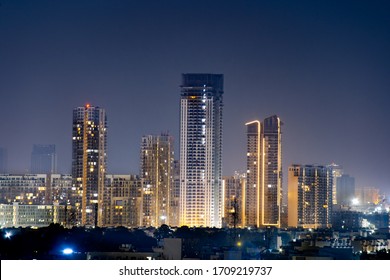 High rise multi story skyscrapers lit up at night with small houses in the foreground at night in gurgaon delhi. Shows the rapid pace of development of the real estate sector with property, offices