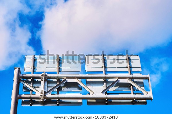 A high road sign\
from thick metal and a complex construction against the backdrop of\
the blue sky and clouds