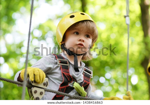 High ropes walk. Helmet and safety equipment.\
Child concept. Happy Little child climbing a tree. Rope park -\
climbing center. Active\
children
