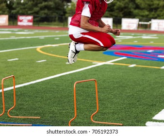 A High School Athlete Jumping Over Hurdles On A Green Turf Field During Pre-season Football Practice.