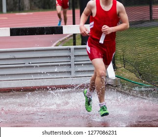 A High School Boy Is Exiting The Water Pit While Running A Race In The 3000 Meter Steeplechase Event.