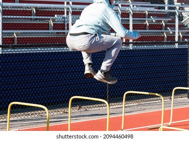 High School Boy Jumping Over Two Foot Tall Yellow Hurdles In Front Of Bleachers During Track And Field Agiity And Strength Practice