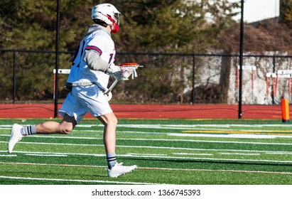 A high school boy lacrosse player is running doen the field with the ball in the net of his stick looking to make a play. - Powered by Shutterstock