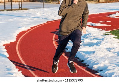 A High School Boy Is Running On A Track In Lane One With The Rest Of The Track Covered With Snow During Winter Track And Field Practice.