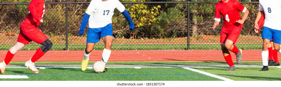 High School Boys Controlling The Ball During A Soccer Game On A Green Turf Field.