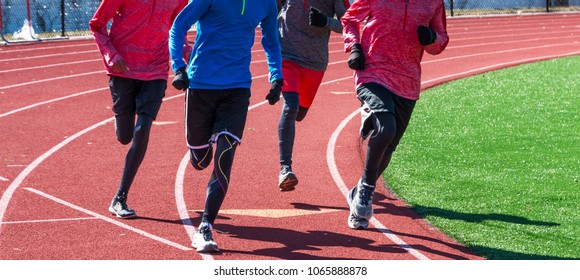 High School Boys Run A Workout Together Wearing Gloves And Spandex On A Red Track During Winter Track And Field Practice.