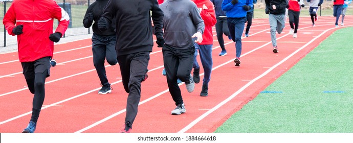 A High School Boys Winter Track Team Running On A Track Covered Up With Spandex And Sweatpants On Their Legs, Sweatshirts And Gloves To Help Keep Them Warm.