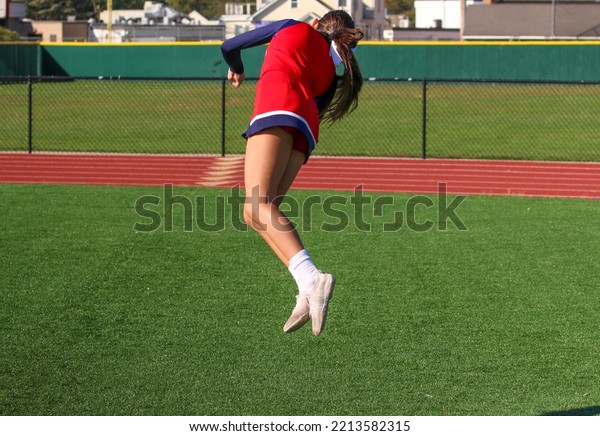 A high school cheerleader is\
twisting midair while warming up for pep rally on a turf\
field.