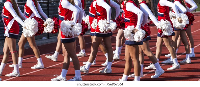 High school cheerleaders cheering on the crowd at a football game on a sunny afternoon in the fall.