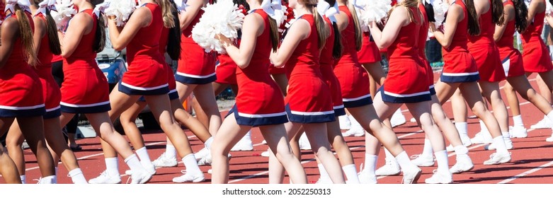 High School Cheerleaders Wearing Red And White Uniforms Cheering While Holding Pom Poms During A Homecoming Football Game.