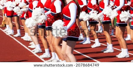 High school cheerleaders wearing red and white uniforms cheering on the sidelines of a football game