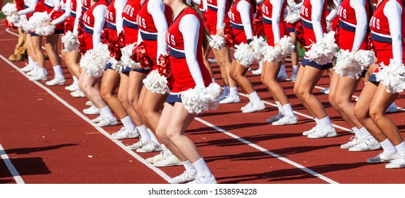 A High School Cheerleading Team Is Synchronized On A Red Track While Performing For The Fans Furing A Football Game. 