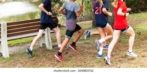 High school cross country runners running together around a lake on grass in a park.