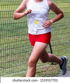 A high school female cross country runner in a white and red uniform running next to a wire fence during a 5K race.